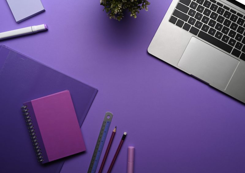 Flat lay computer laptop, potted plant and stationery on purple background.